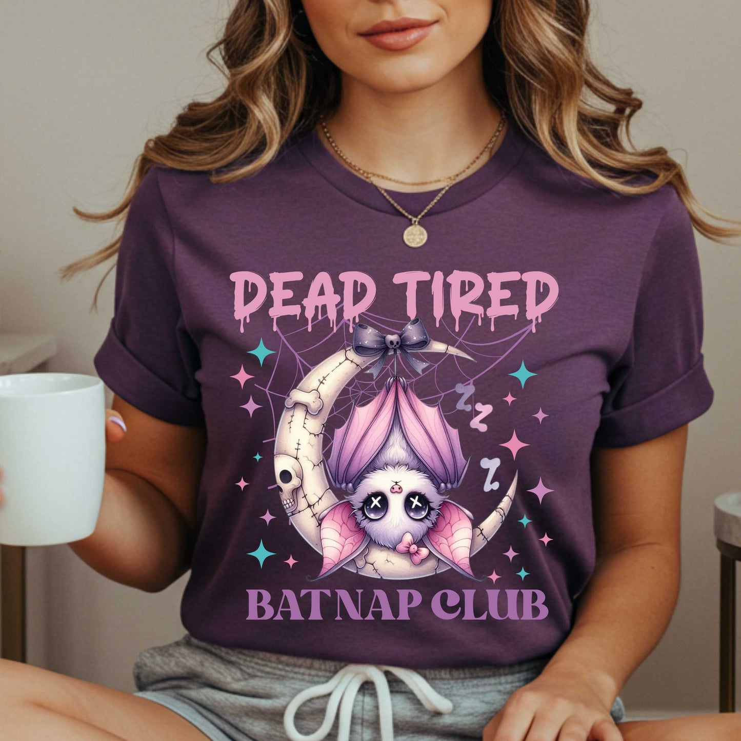 Dead tired and fully over it? Same. Join the Batnap Club with this pastel goth bat Halloween shirt, featuring a sleepy little winged gremlin who’s clearly clocked out. Wrapped in a pink bow and hanging like tomorrow’s problems, this adorable burnout bat is all of us in October (and every Monday). Perfect for spooky naps, haunted errands, or just surviving on caffeine and vibes. 