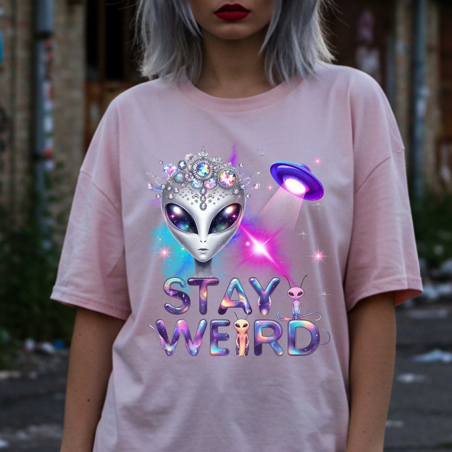Beam us up, queen—the galaxy’s weirdest and most fabulous fashion icon has entered the orbit. This Stay Weird alien graphic tee is here to remind Earthlings that normal is overrated. Featuring a cosmic glam alien with jeweled headgear and a full-on abduction spotlight moment, this shirt is serving interstellar weirdness with a side of sparkle. 
