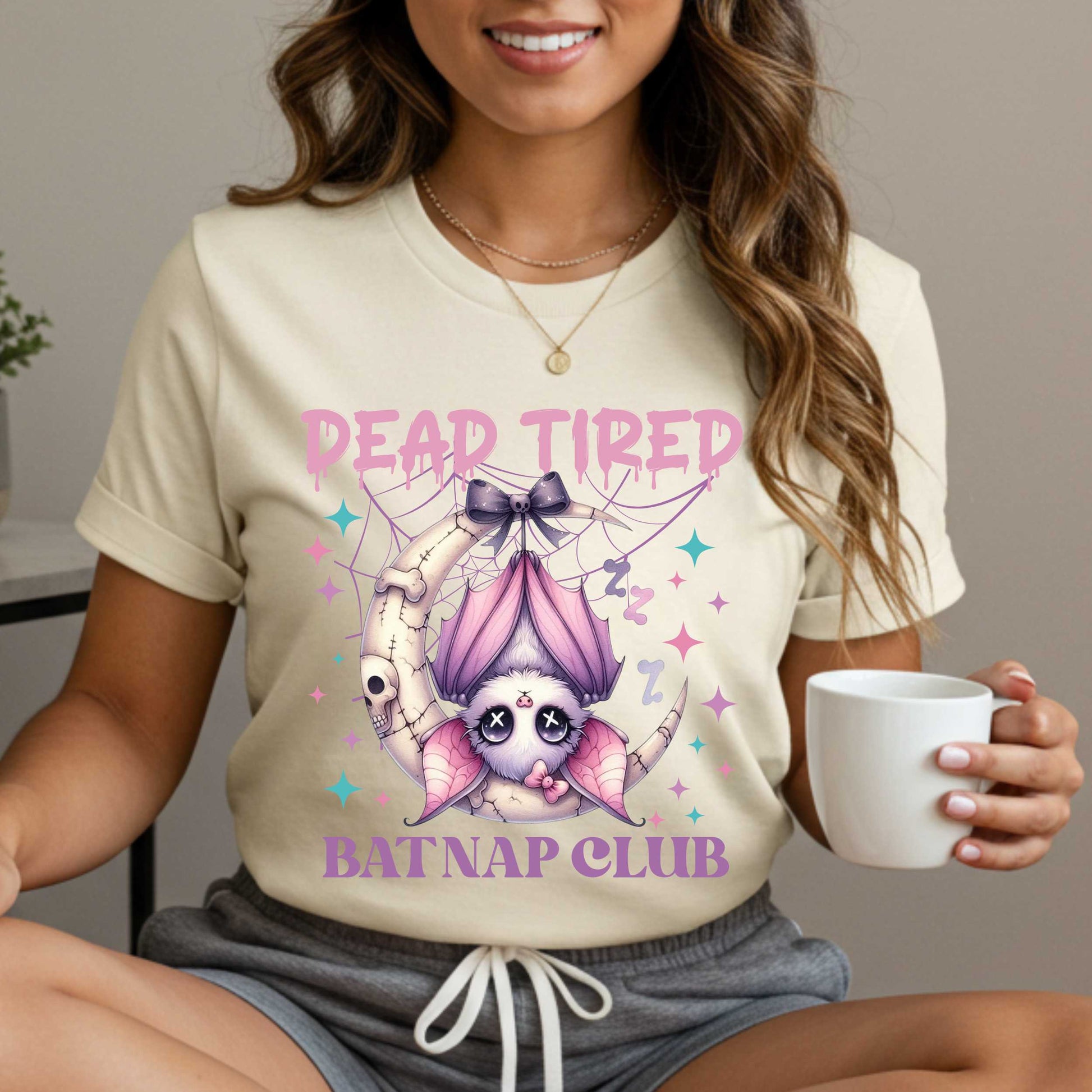 Dead tired and fully over it? Same. Join the Batnap Club with this pastel goth bat Halloween shirt, featuring a sleepy little winged gremlin who’s clearly clocked out. Wrapped in a pink bow and hanging like tomorrow’s problems, this adorable burnout bat is all of us in October (and every Monday). Perfect for spooky naps, haunted errands, or just surviving on caffeine and vibes.&nbsp;
