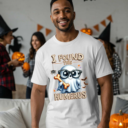 Bone-afide hilarious. This “I Found This Humerus” tee is the ultimate Halloween dad joke wrapped in spooky cute style. Featuring a ghost rocking nerdy glasses and proudly holding a humerus bone like it just cracked itself up—because it did. 