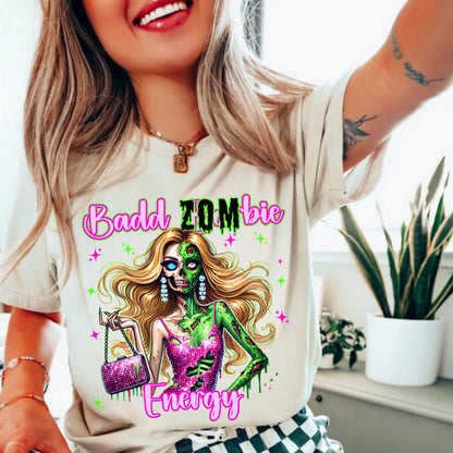 Brains, but make it fashion. This Badd Zombie Energy tee is for the girls who slay… even in the afterlife. Rocking a glittery pink dress, designer handbag, and enough undead glam to raise the dead, this zombie babe is dripping in sass (and maybe a little ooze).